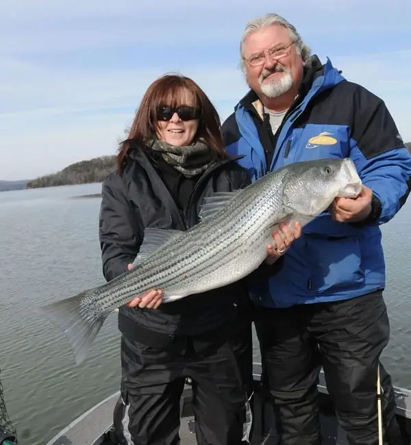 A man and woman holding a striped bass on the water.